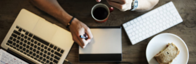 Man writing at desk with laptop and coffee